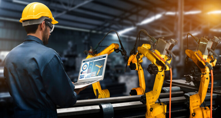 Worker in a hard hat holding a laptop monitoring pick-and-place machines